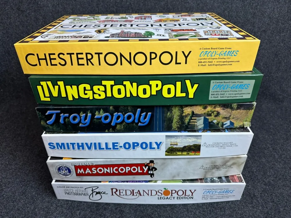 A stack of custom Townopoly game boxes: Chestertonopoly, Livingstonopoly, Troy-opoly, Smithville-Opoly, Masonicopoly, and Redlandsopoly