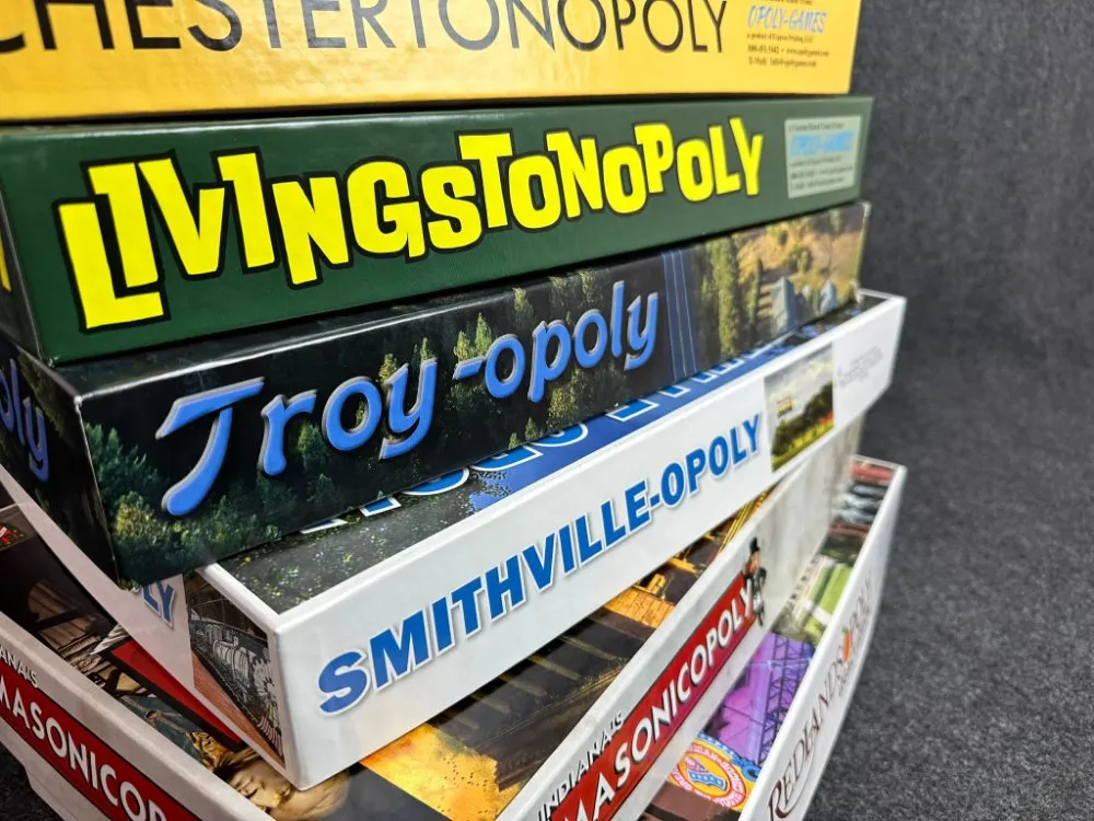 A stack of custom Townopoly game boxes from different towns